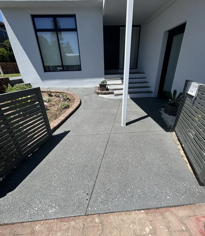 Dark grey resurfaced concrete entry path curving past steps of a modern home