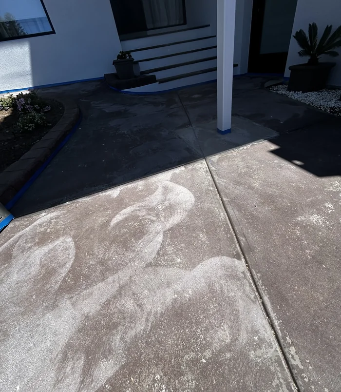Stained concrete entry path with blue masking tape beside a modern home, before resurfacing