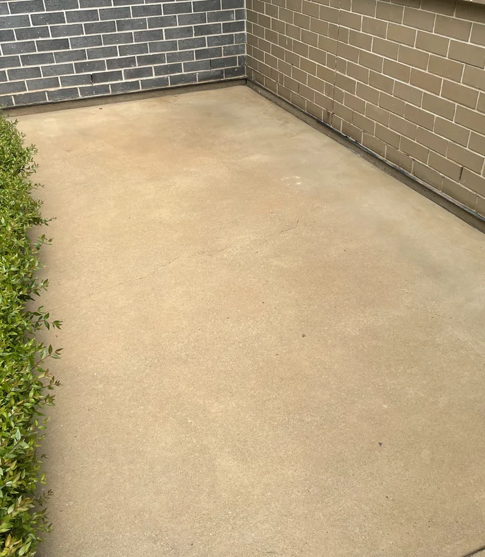 Clean, even-toned concrete slab beside a grey brick wall after pressure washing