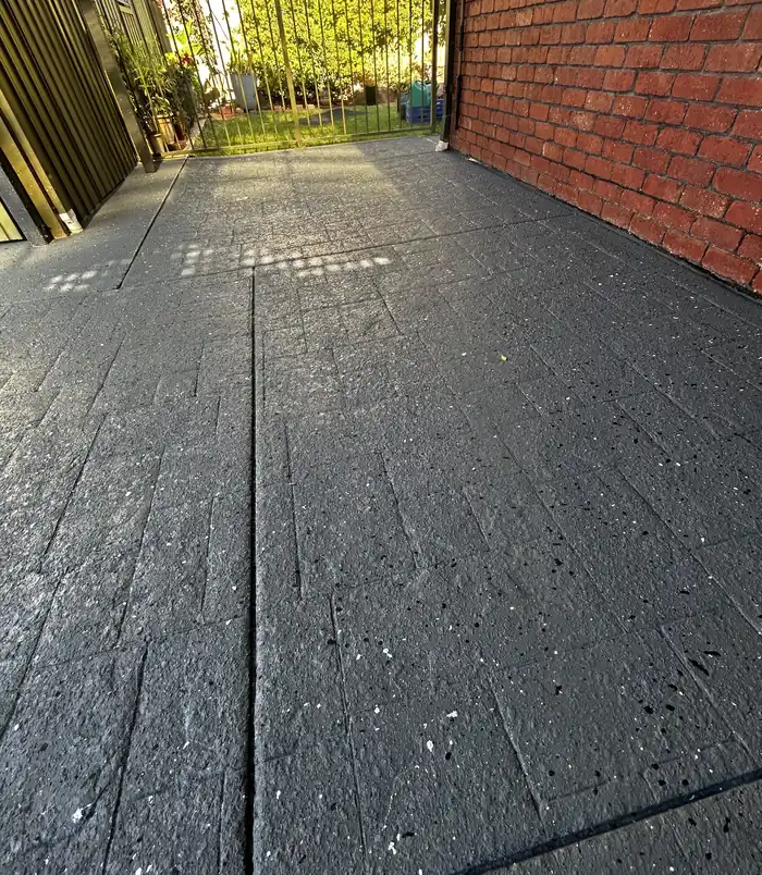 Even grey resurfaced stamped-pattern concrete patio beside a brick wall
