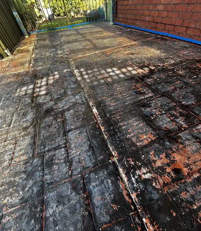 Stained, worn stamped-pattern concrete patio beside a brick wall, before concrete resurfacing