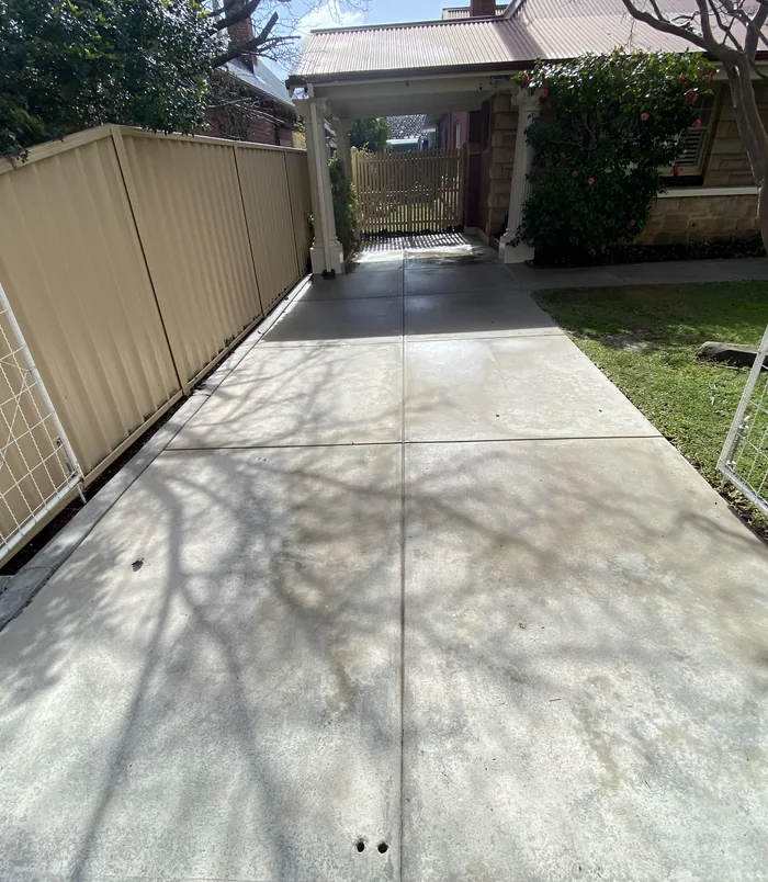 Clean, light concrete driveway beside a tan fence and carport after pressure washing