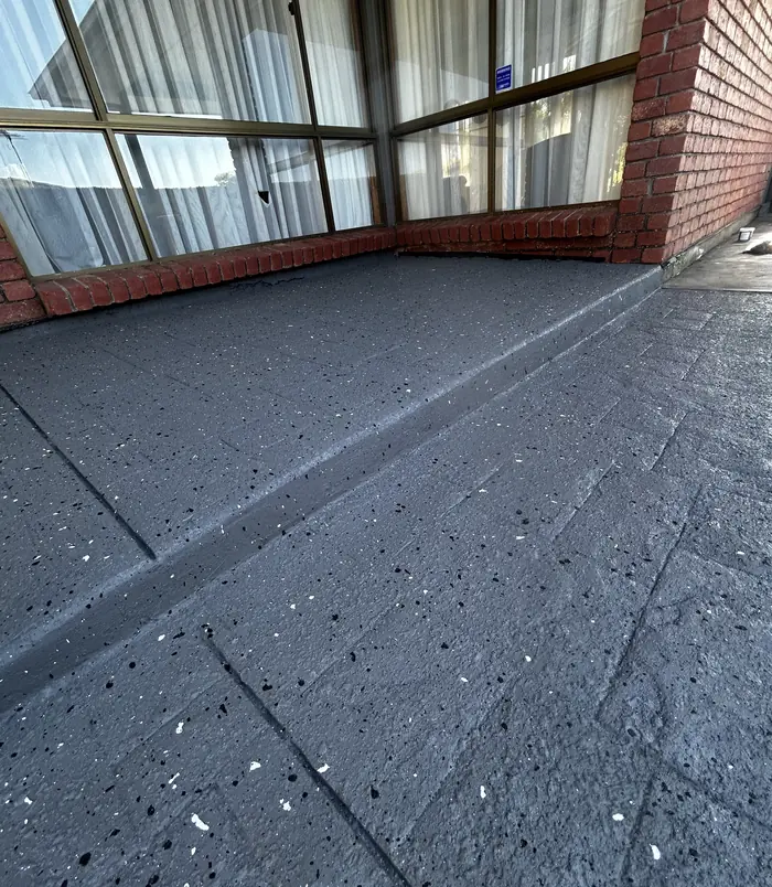 Smooth dark grey resurfaced stamped concrete beside a brick wall and glass doors