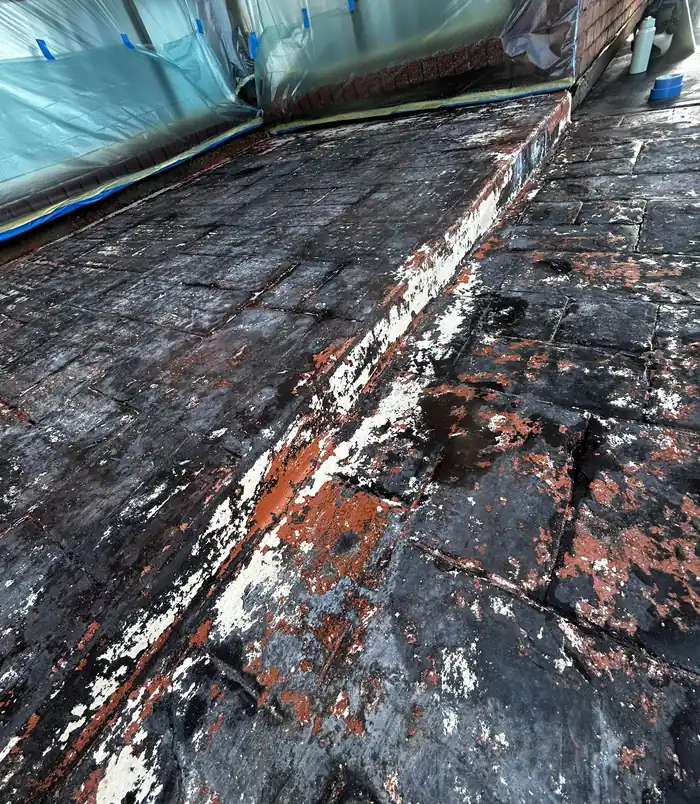 Black, patchy stamped concrete with peeling coating and blue tape, before concrete resurfacing