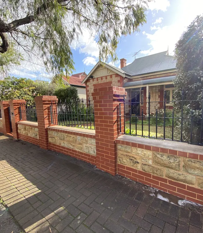 Clean stone and brick front fence in front of a heritage home after pressure washing