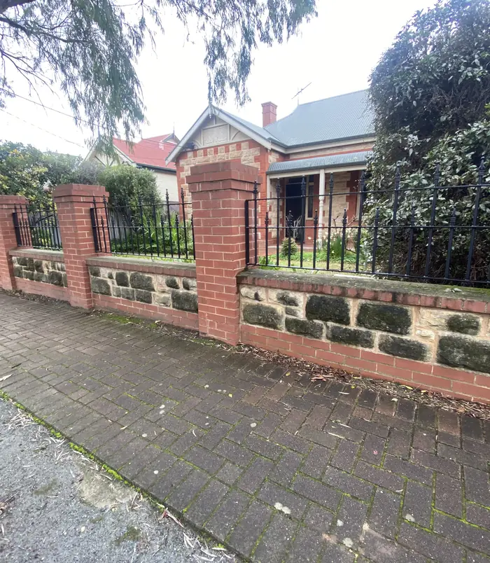 Dirty stone and brick front fence in front of a heritage home, before pressure washing