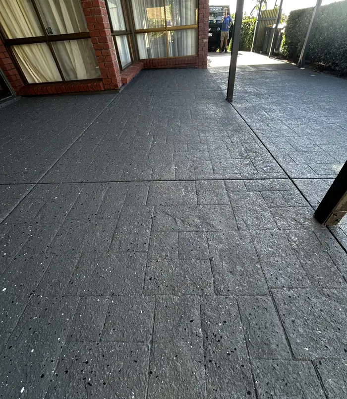 Dark grey resurfaced stamped-pattern concrete patio beside a brick wall and glass doors