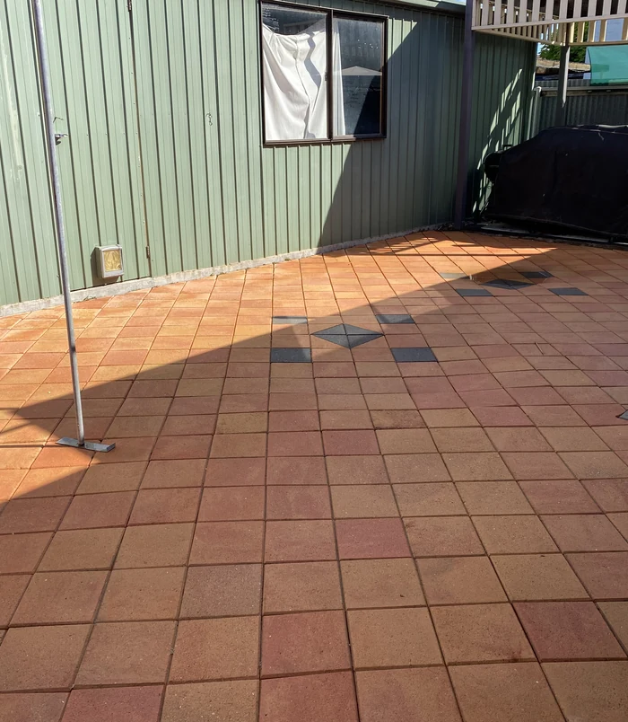 Terracotta pavers with dark accent tiles beside a green wall, restored to bright colour after pressure washing