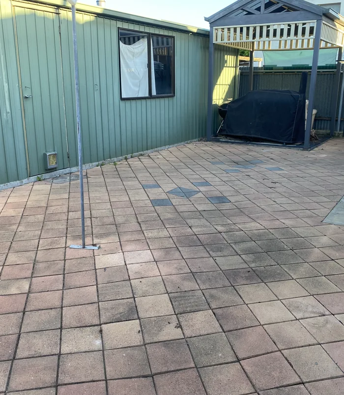 Faded, dirty pavers beside a green weatherboard wall, before pressure washing
