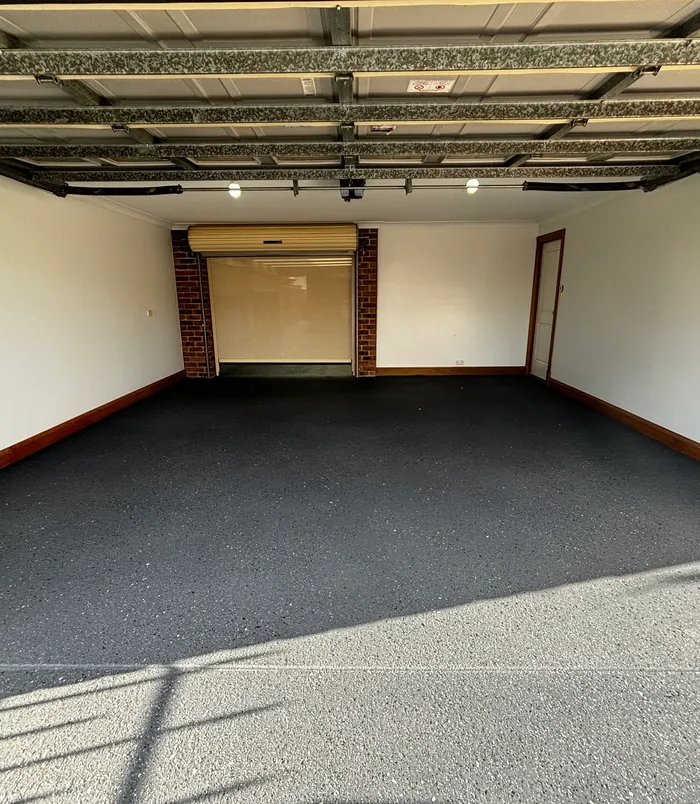 Dark resurfaced concrete garage floor with a roller door and brick pillars