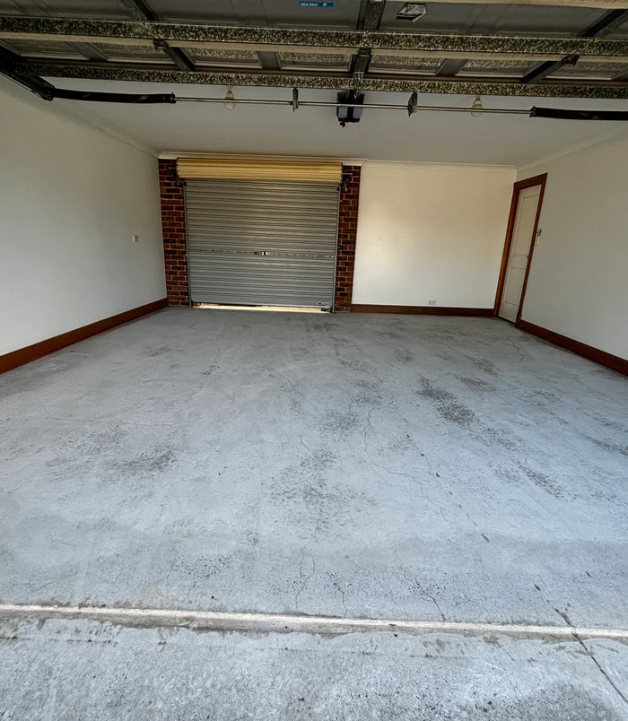 Pale, worn concrete garage floor with a roller door and brick pillars, before concrete resurfacing