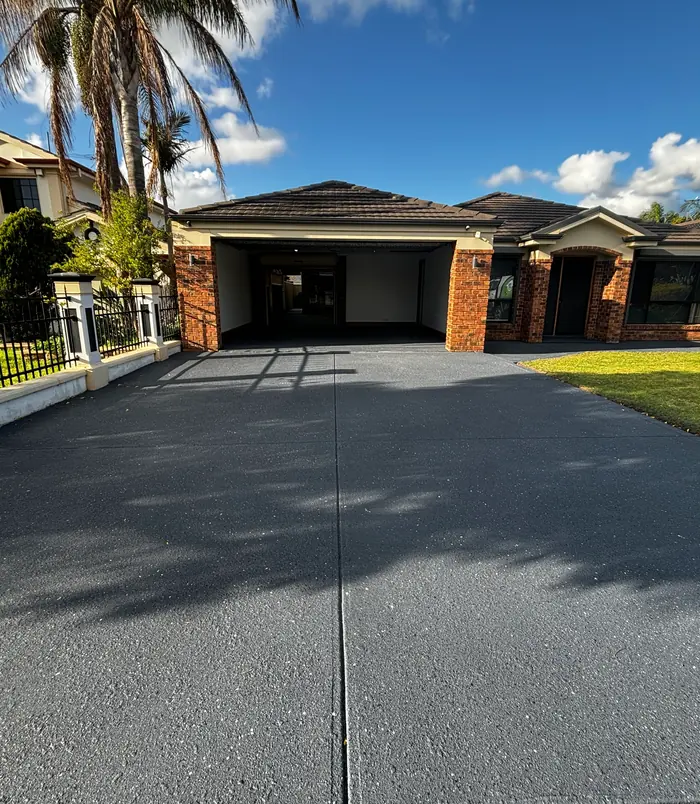 Dark resurfaced concrete driveway leading to a double garage with brick pillars