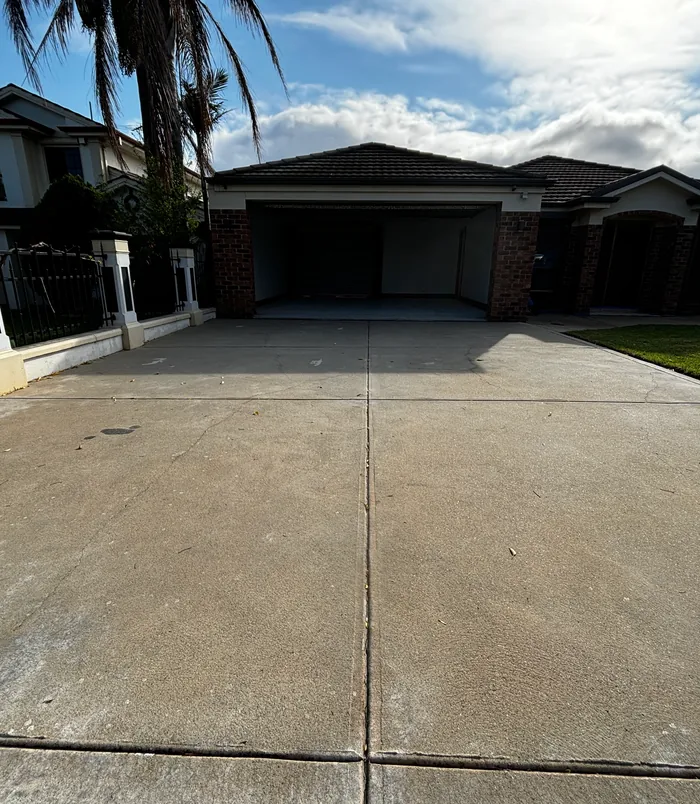 Stained, uneven concrete driveway leading to a double garage with brick pillars, before resurfacing