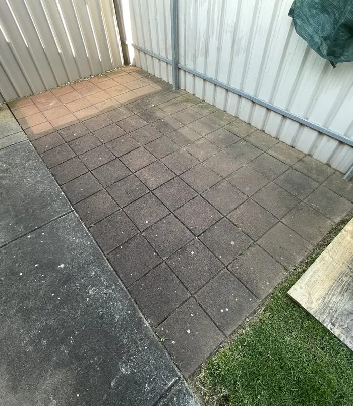 Dark, dirty square pavers in a courtyard beside a metal fence, before pressure washing