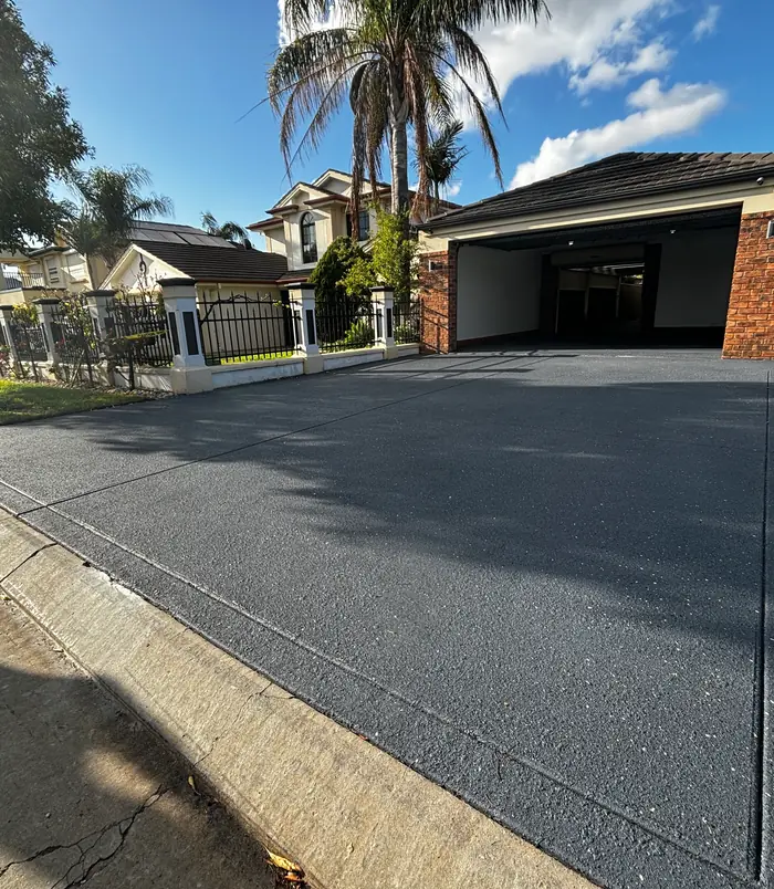 Dark grey resurfaced concrete driveway in front of a double garage and palm trees
