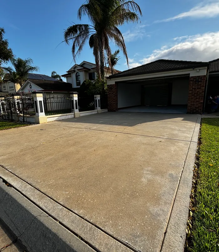 Pale, weathered concrete driveway in front of a double garage and palm trees, before concrete resurfacing