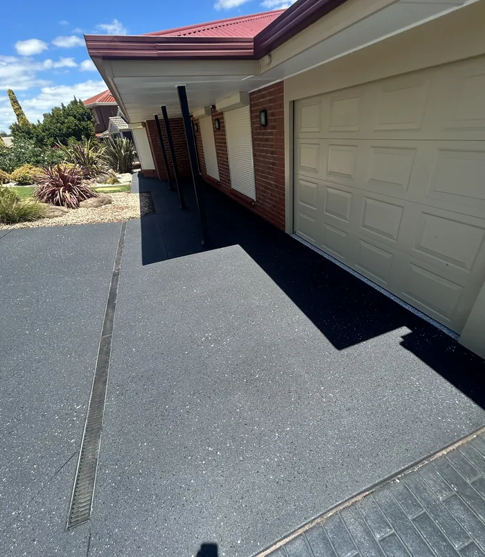 Dark grey resurfaced concrete path beside a brick home and cream garage door
