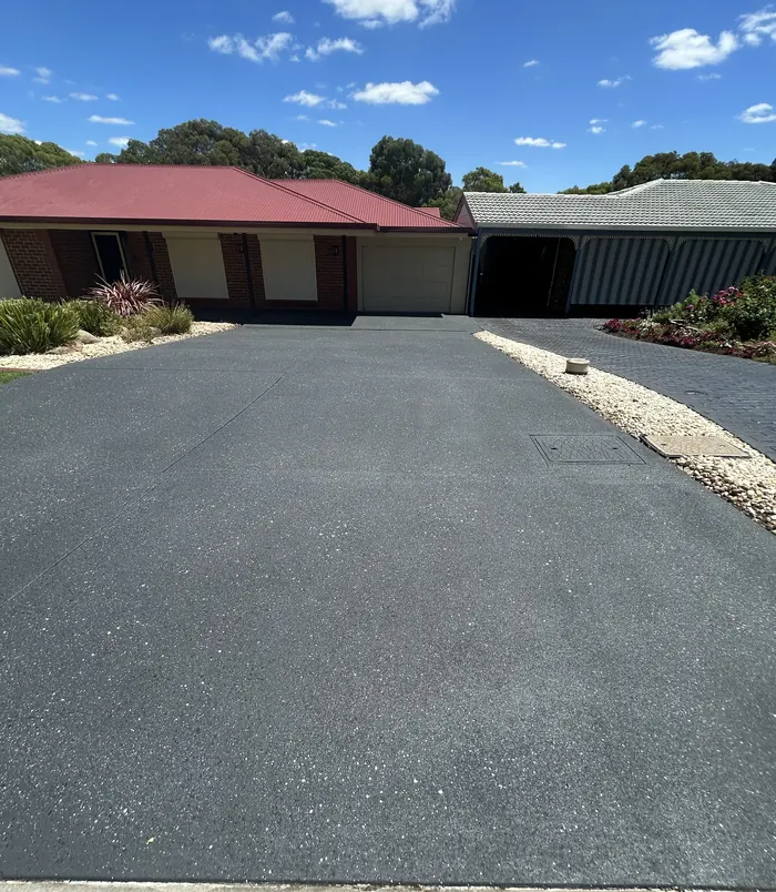 Dark grey resurfaced concrete driveway curving past a gravel garden in front of a brick home