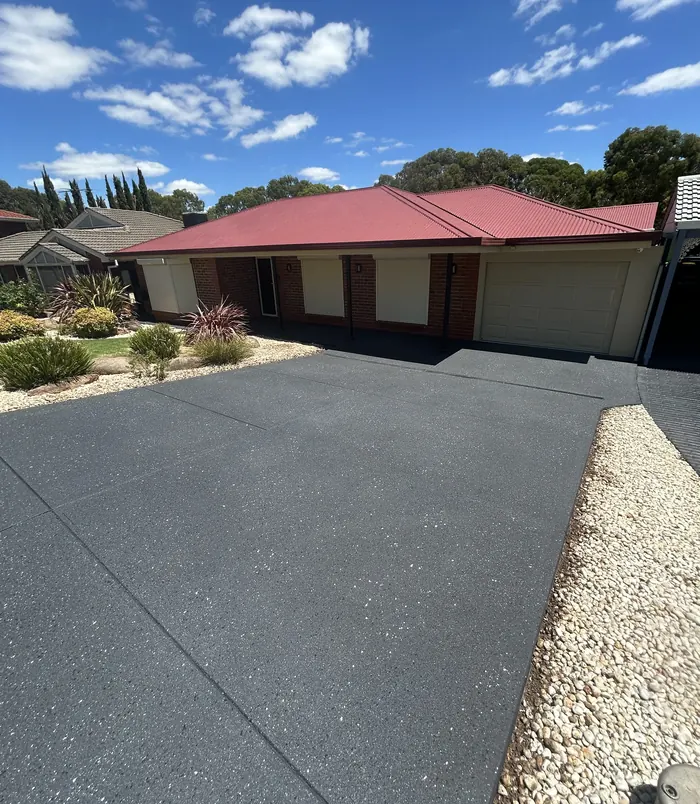 Dark grey resurfaced concrete driveway in front of a brick home with a red roof
