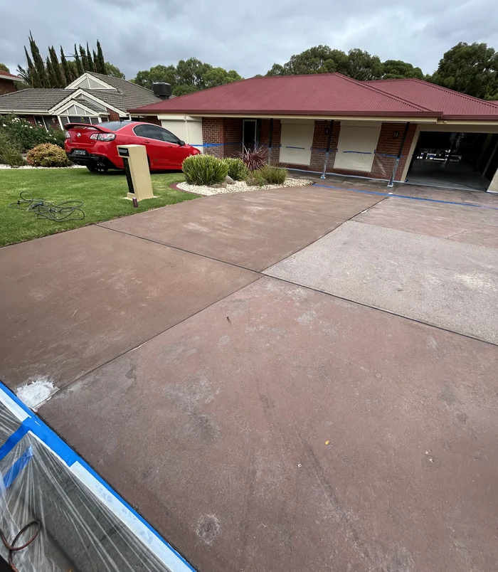 Faded, patchy red and pink concrete driveway in front of a brick home with a red roof, before resurfacing