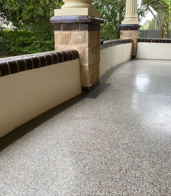 Clean, glossy concrete walkway beside a rendered wall with sandstone pillars after pressure washing