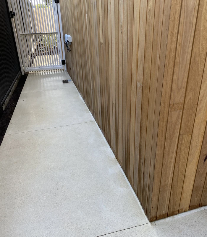 Clean, light concrete side path beside a timber fence and gate after pressure washing