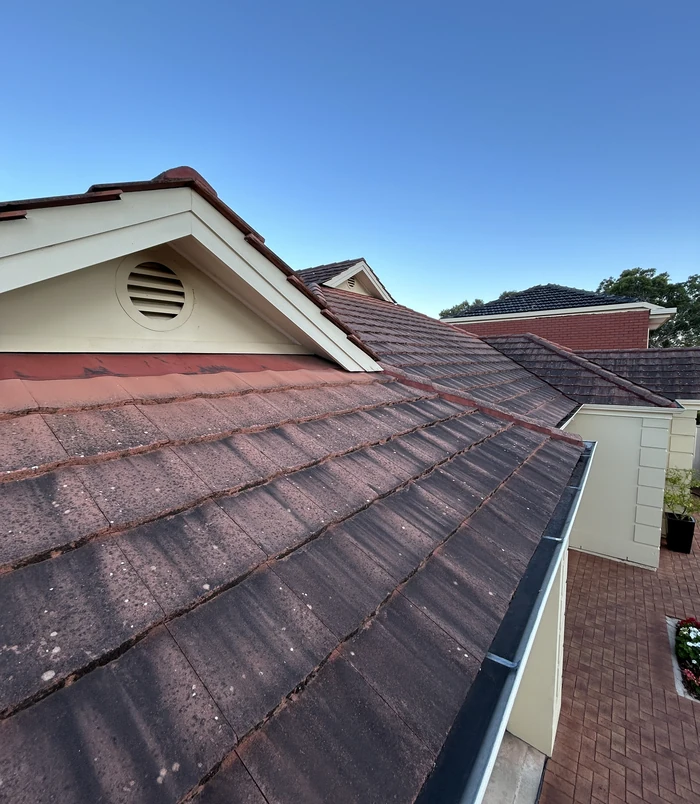 Dull, weathered terracotta roof tiles under a blue sky, before pressure washing