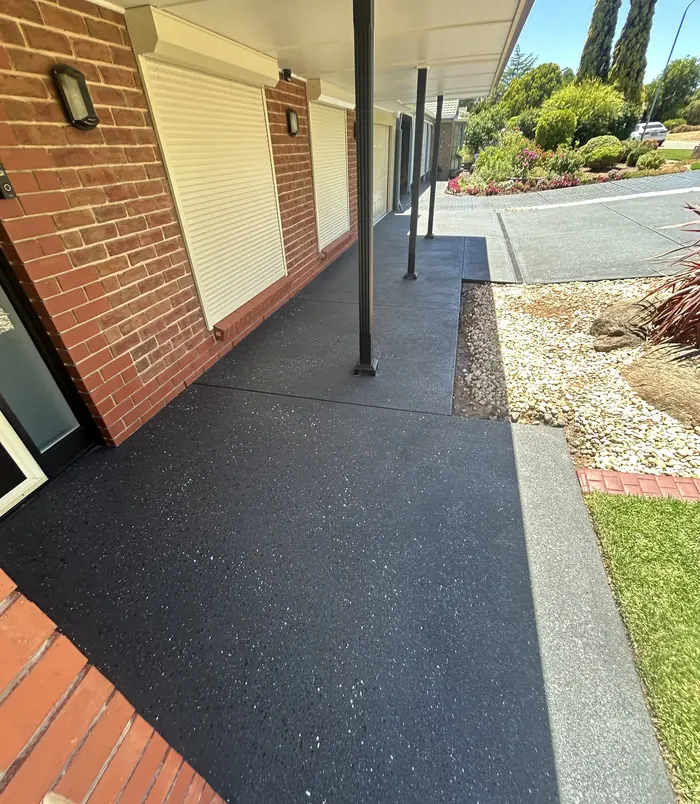 Dark grey resurfaced concrete path beside a brick wall, veranda posts and gravel garden