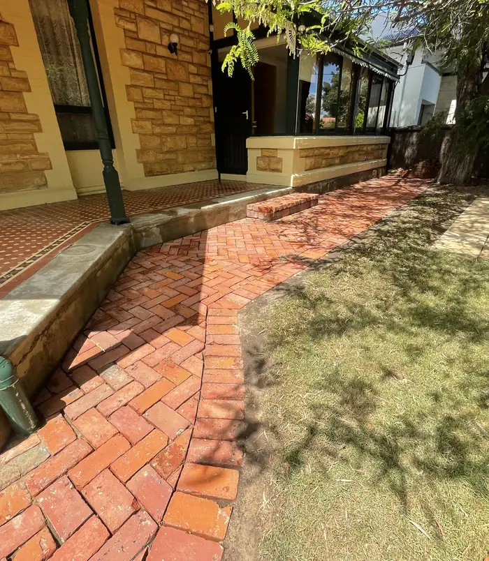 Clean red brick paving beside a sandstone house after pressure washing