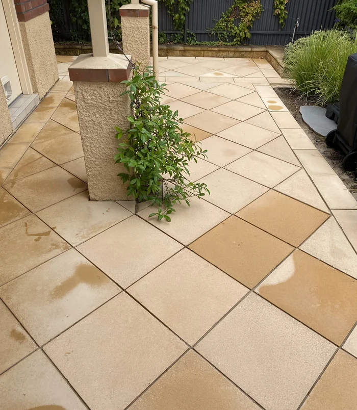 Clean, golden diamond-pattern pavers around a stone pillar with a climbing plant after pressure washing