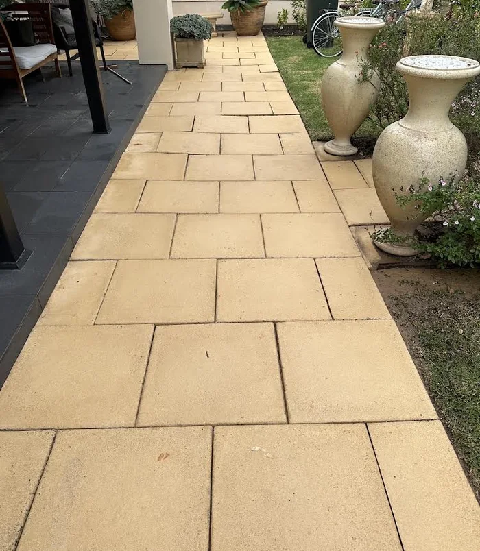 Clean, golden-toned paved pathway beside a garden with large urns after pressure washing