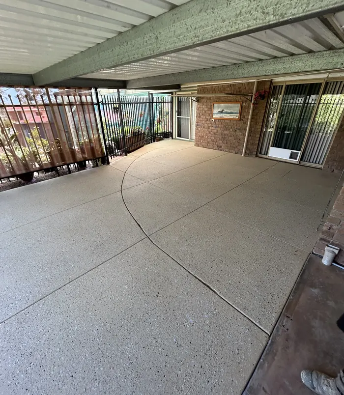 Clean, even resurfaced concrete patio under a pergola beside a brick wall
