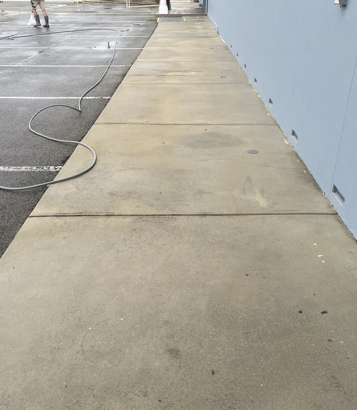 Clean concrete path beside a house wall with a hose alongside, after pressure washing