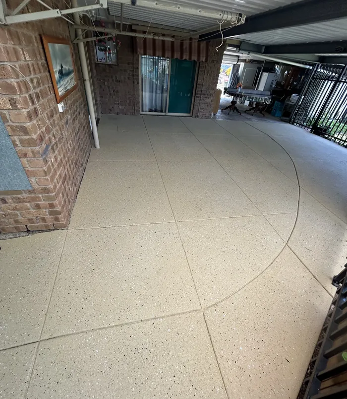 Clean, uniform resurfaced concrete patio beside a brick wall and glass door
