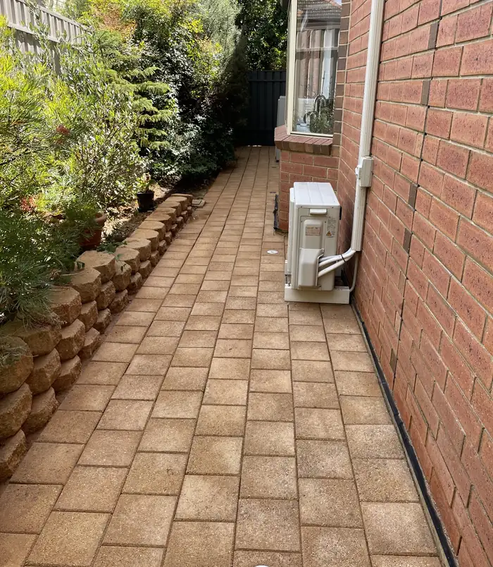 Brick pavers beside a red brick wall and air conditioner, restored to warm colour after pressure washing