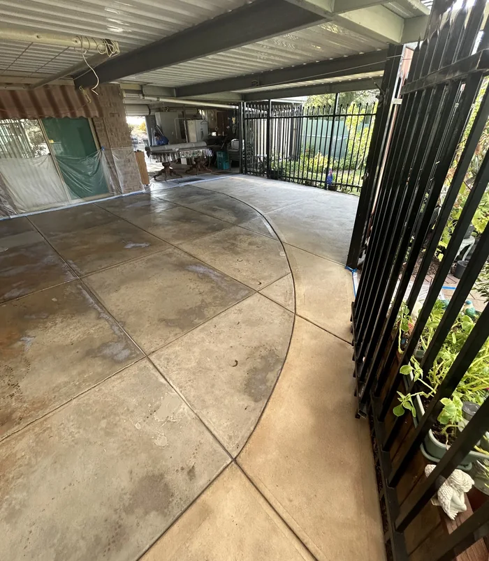 Stained, patchy concrete courtyard beside a black metal fence before resurfacing
