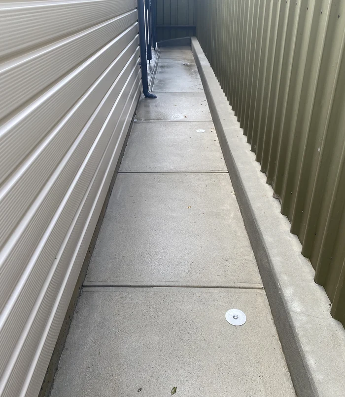 Clean, light concrete side path beside a house wall and fence after pressure washing