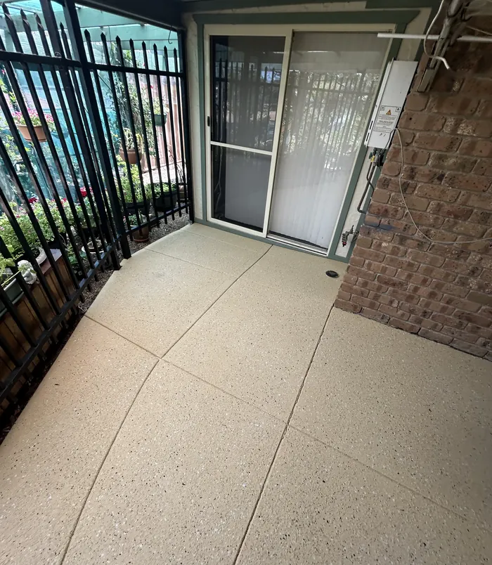 Clean, light resurfaced concrete entry beside a black fence and glass door