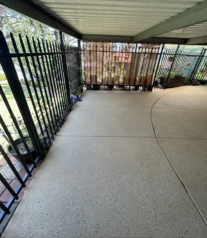 Clean, even resurfaced concrete courtyard under a pergola beside a black metal fence