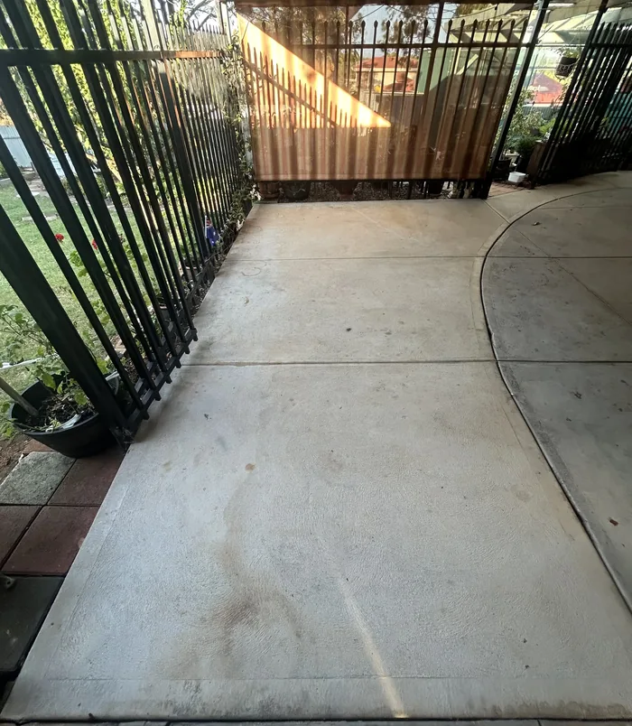 Stained, patchy concrete courtyard beside a black metal fence and timber screen, before resurfacing
