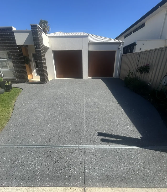Dark grey resurfaced concrete driveway in front of a modern home with brown garage doors