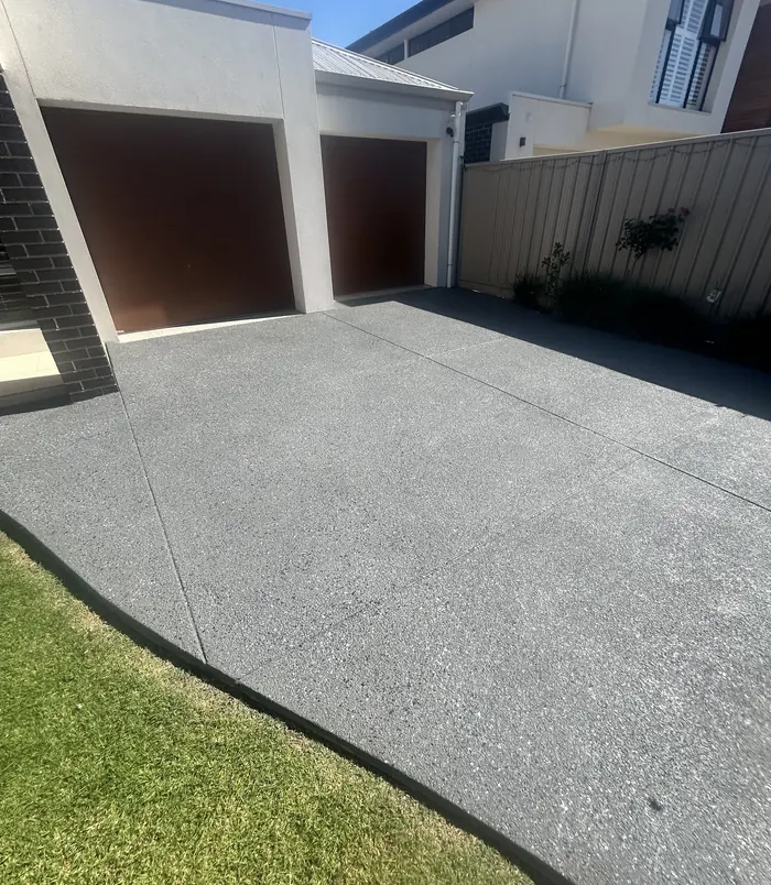 Dark grey resurfaced concrete driveway in front of a garage with brown doors