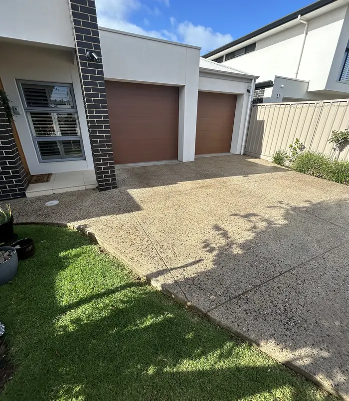 Dull, rough exposed aggregate driveway in front of a double garage with brown doors, before resurfacing