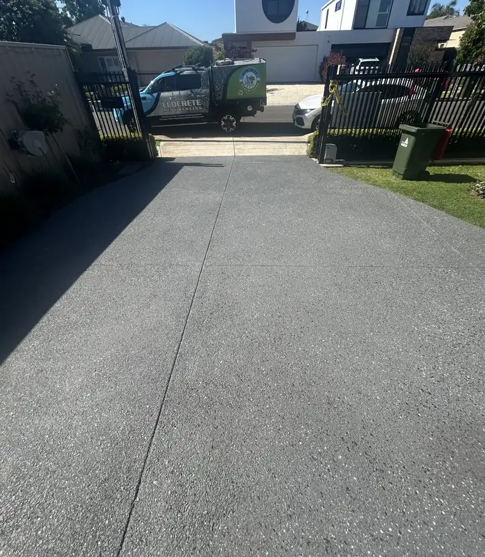 Dark grey resurfaced concrete driveway leading to a gate and fence