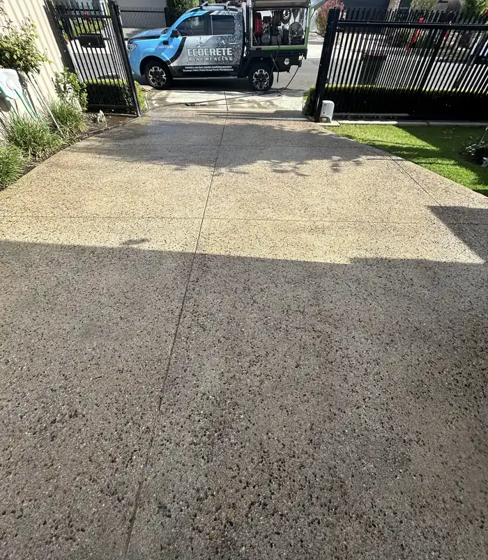 Pale, weathered exposed aggregate driveway leading to a gate and fence, before concrete resurfacing
