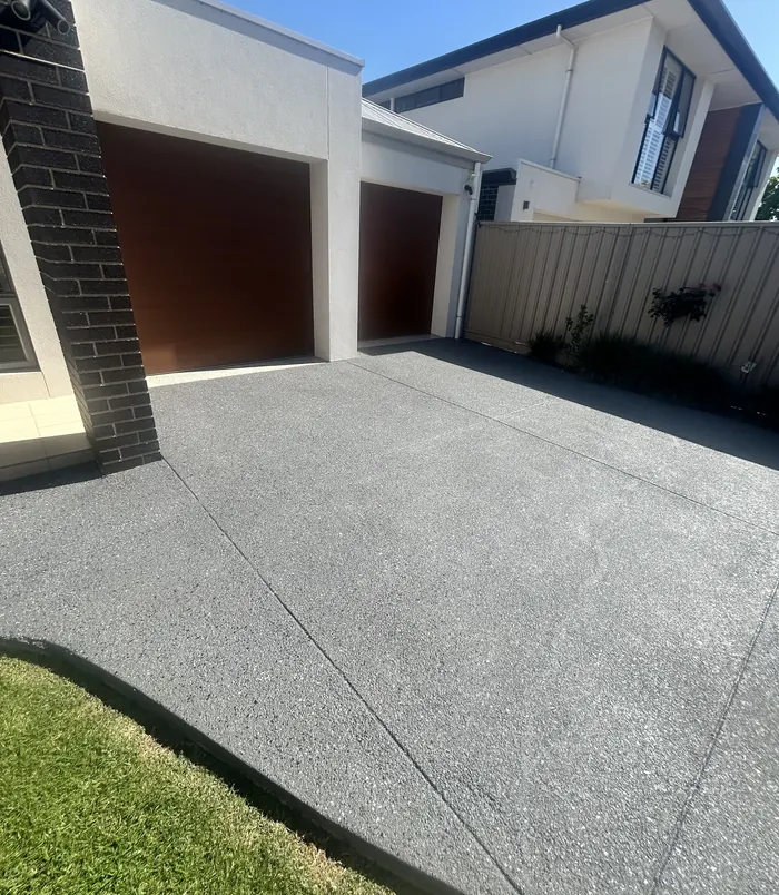 Dark grey resurfaced concrete driveway in front of a double garage with brown doors