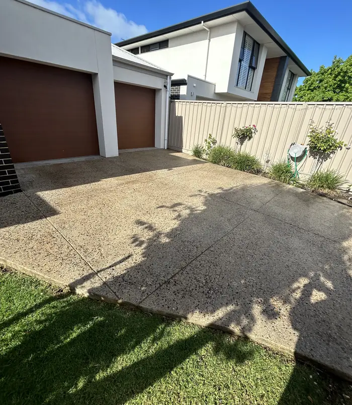 Dull, rough exposed aggregate driveway in front of a double garage with brown doors, before resurfacing