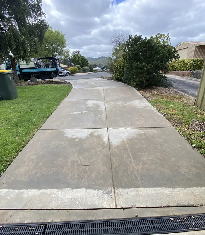 Clean, light grey concrete driveway beside a grass verge after pressure washing
