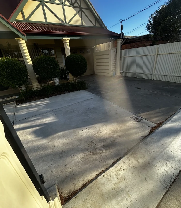 Pale, stained concrete driveway in front of a character home with columns, before resurfacing