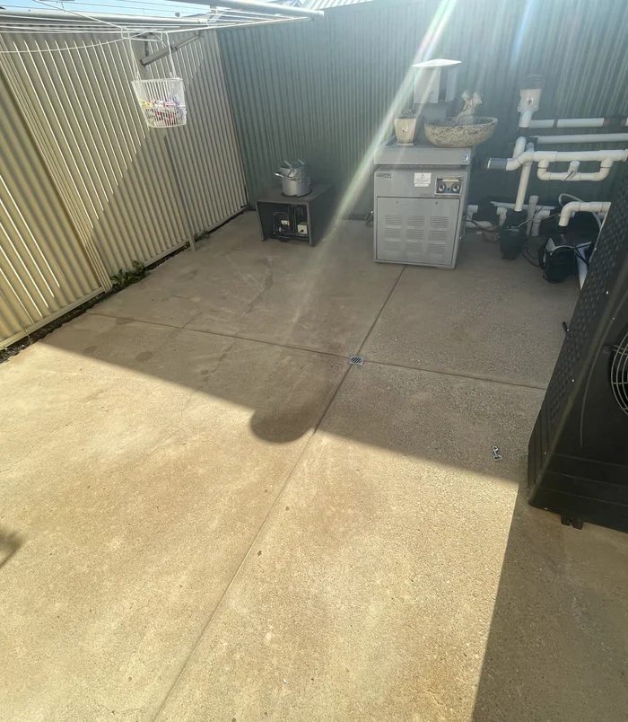 Clean concrete courtyard beside a fence with a pool pump and equipment, after pressure washing